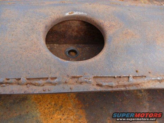 Close-up of heavily rusted metal with a circular opening and visible weld marks