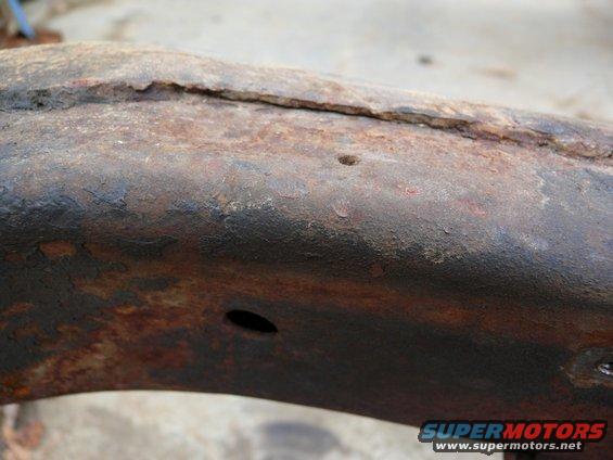 Rusted metal frame section with two holes, showing corrosion and wear