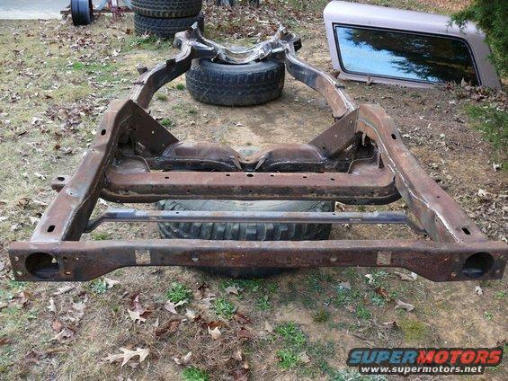 Rusted vehicle frame with two tires visible underneath and a truck cap in the background