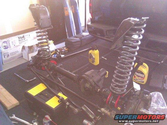 Front axle assembly with coil springs and shock mounts, tools, and oil bottles on a garage floor