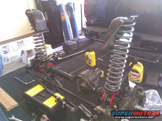 Vehicle suspension parts, including springs and axles, laid out on a garage floor