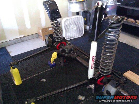 Front axle assembly with shocks and springs on a black mat. Yellow fluid bottle visible
