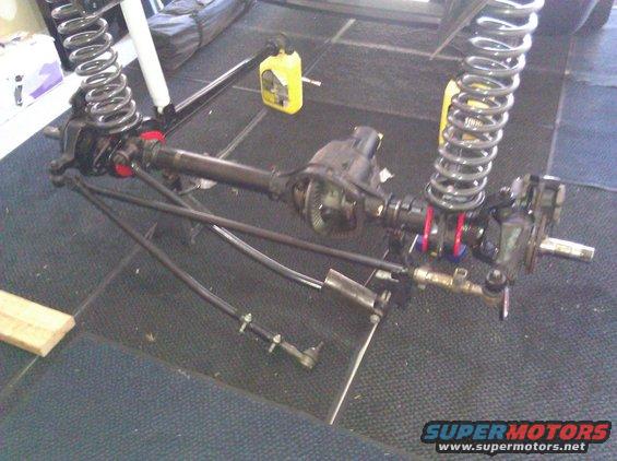 Front axle assembly with coil springs, shocks, and steering components laid out on a carpeted floor