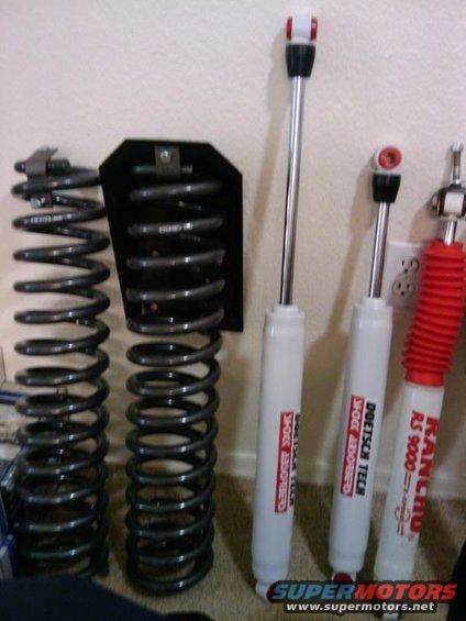Two coil springs and three shock absorbers are laid out on the floor