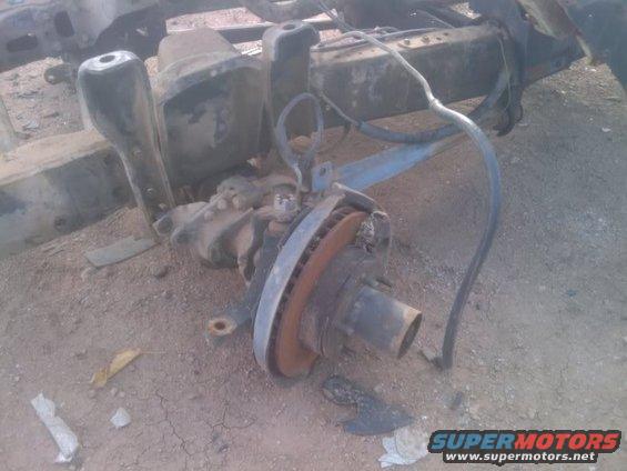 Front axle assembly with rusty brake rotor and suspension parts on the ground