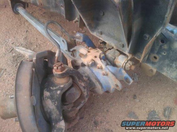 Close-up of rusty vehicle suspension parts, including a ball joint and control arm, on a dirt surface