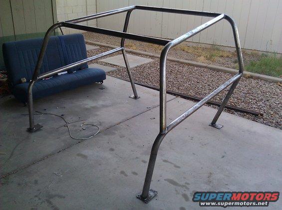 Custom metal roll cage frame on concrete, with a blue vehicle seat in the background