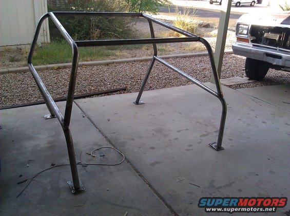 Custom metal roll cage frame on concrete driveway. Part of a vehicle is visible in the background