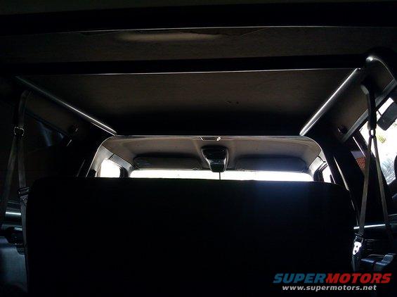 Interior view of a vehicle's rear seats and roll cage structure. A "SUPERMOTORS.NET" watermark is visible