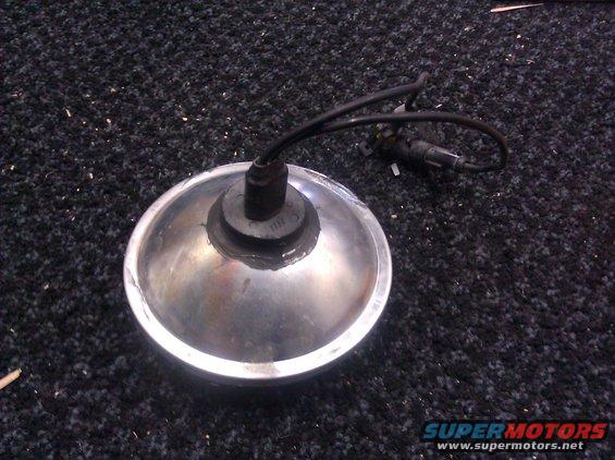 Headlight assembly with chrome trim and black wiring, resting on a dark carpeted surface