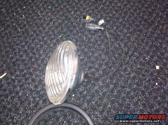 Headlight assembly with clear ribbed lens and wiring harness, lying on a dark carpeted surface