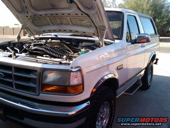 White Ford Bronco with hood open, showing engine. Bronco badge visible on fender