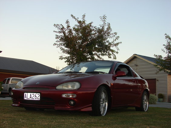Red coupe parked on grass, front 3/4 view. License plate ALA262