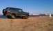 1992 Ford Bronco - A dark 1992 Ford Bronco is parked on a sandy area near the water, with a spare tire mounted on the rear.