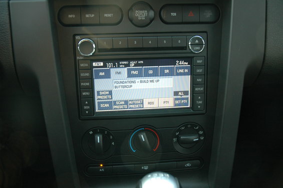 Car dashboard showing radio display with song title, climate controls, and gear shift