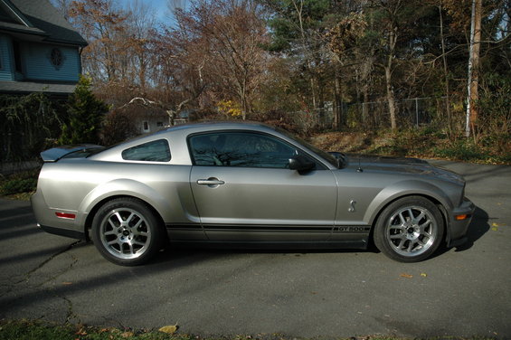 Silver Ford Mustang Shelby GT500 with black side stripes and GT500 badging, parked on asphalt