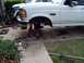 1996 Ford Bronco - Front wheel removed from a white 1996 Ford Bronco undergoing lift installation. Tools and jacks are visible around the vehicle.