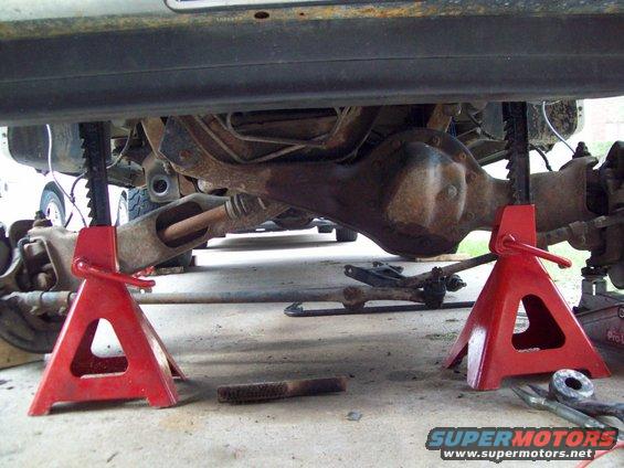 Undercarriage of a vehicle, showing the rear axle and suspension components supported by red jack stands