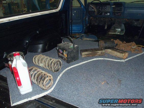 Interior of a blue vehicle with springs, a battery, wooden blocks, and chains on the floor
