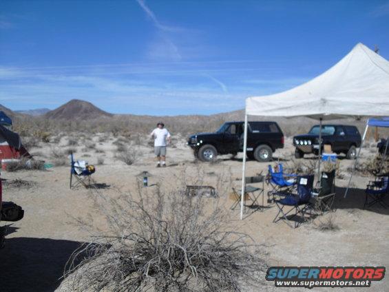Two black Ford Broncos parked in a desert campsite with a tent and chairs