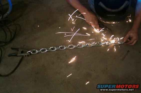 Person welding a metal chain on a concrete floor, sparks flying