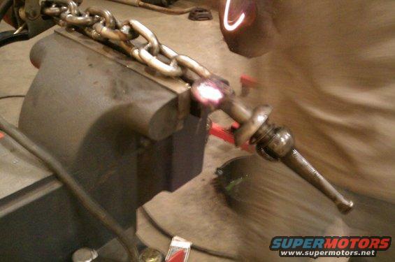 Chain link held in a vise, with a metal rod being heated and glowing red hot