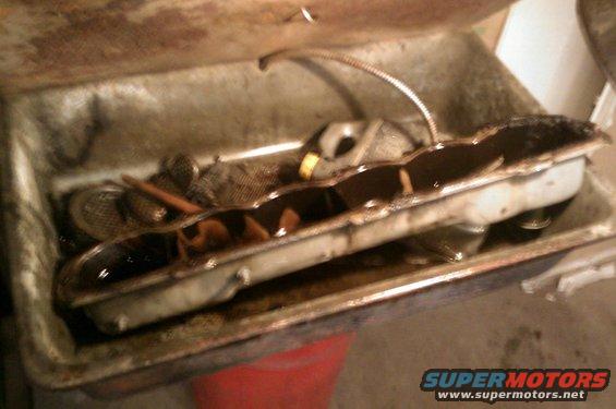 Oil pan with dark oil and a mesh screen inside, sitting in a metal tray