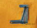 1969 Ford Mustang - Metal bracket with blue paint and two mounting holes, photographed on a textured surface.