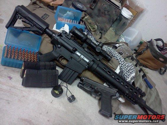 AR-15 style rifle with scope, handgun, and boxes of ammunition on a tactical bag