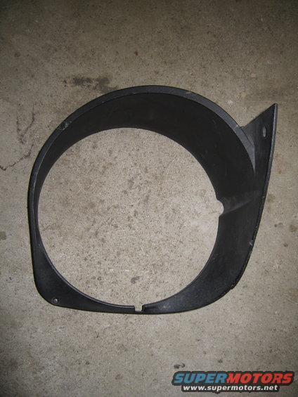 Black plastic headlight bezel with a triangular mounting tab, lying on a concrete surface