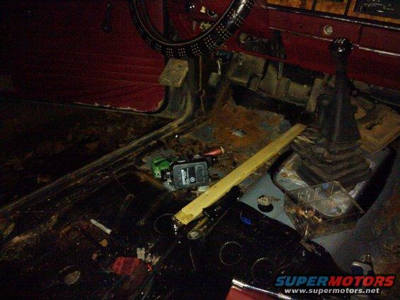Vehicle interior with torn red upholstery, rusted floor, and a gear shifter