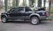 2009 Ford F-150 - A black crew cab pickup truck is parked on a paved surface, carrying an ATV in its bed.