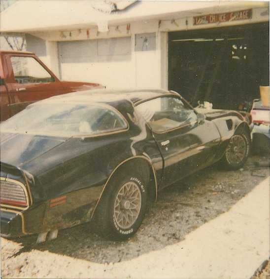 Black 1977 Pontiac Trans Am with gold trim, parked in front of a garage