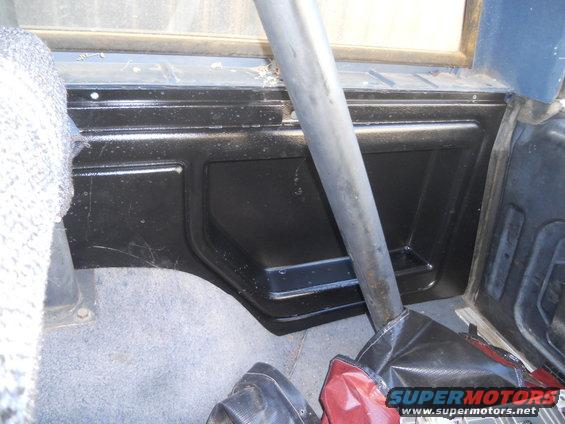 Interior panel and roll bar in a vehicle. Gray carpet and black plastic trim are visible