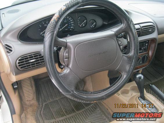 Car interior with a leather-wrapped steering wheel, dashboard gauges, and tan upholstery. A timestamp reads 11/22/2011 14:27