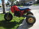 1985 Honda ATC 250 R - A red and blue 1985 Honda ATC 250 R three-wheeler is parked on a lawn next to a driveway.