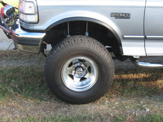 Front wheel and fender of a 1994 Ford Bronco XL, showing the tire, rim, and part of the bumper and grille
