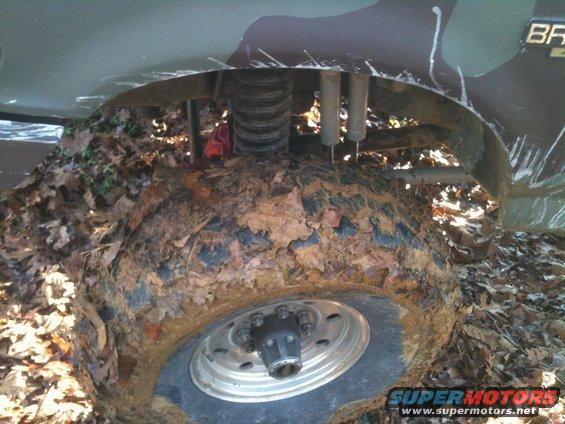 1995 Ford Bronco front wheel deep in mud and leaves, showing suspension components
