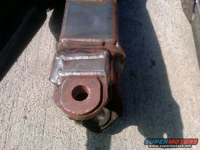 Close-up of a welded metal bracket with a circular hole, resting on concrete