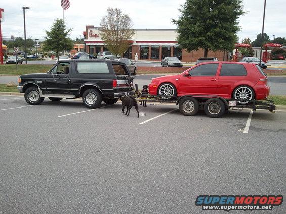 Black 1989 Ford Bronco side view, towing a red Volkswagen Golf