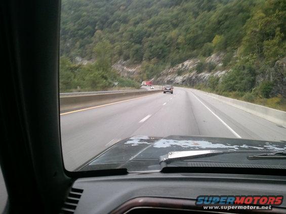 View from inside a vehicle driving on a highway with trees and a rocky hillside