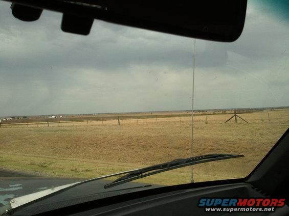 View from inside a vehicle looking out at a dry, grassy field under a cloudy sky. Windshield wipers are visible