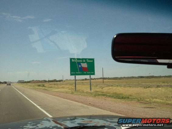 Texas state line sign seen from a vehicle's dashboard, with a rearview mirror visible