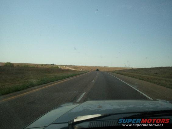 Car hood on highway with distant vehicle under clear sky