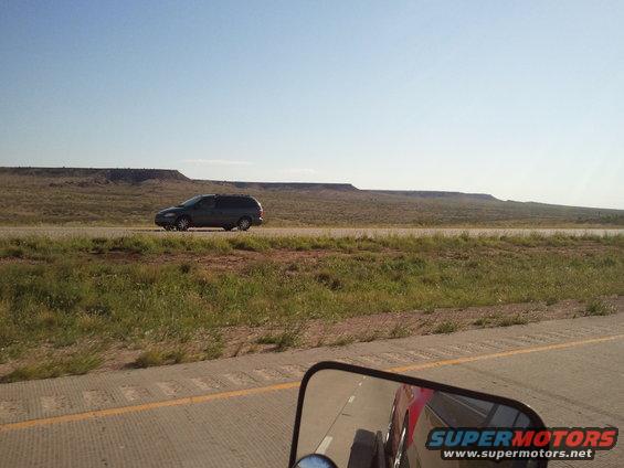 Dark minivan driving on highway; reflection of red car in side mirror