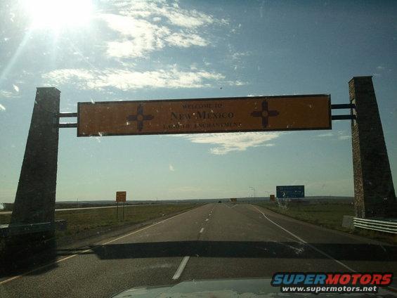 Driving under welcome sign into New Mexico. Sun is bright in the sky