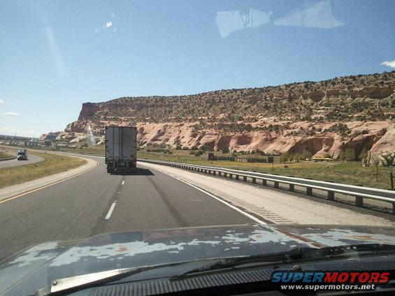 View from inside a vehicle looking at a highway with a semi-truck ahead and mountains in the background