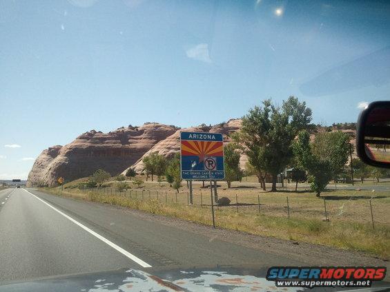 View from car entering Arizona, showing state welcome sign and red rock formations