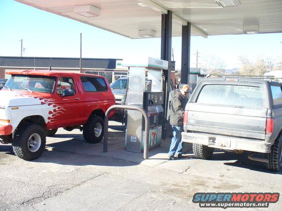 Red and white Ford Bronco with flame decals parked at a gas station