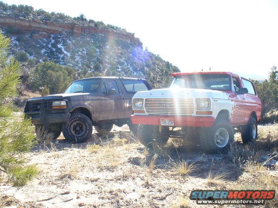 1979 Ford Bronco with red and white paint, parked next to a darker Bronco